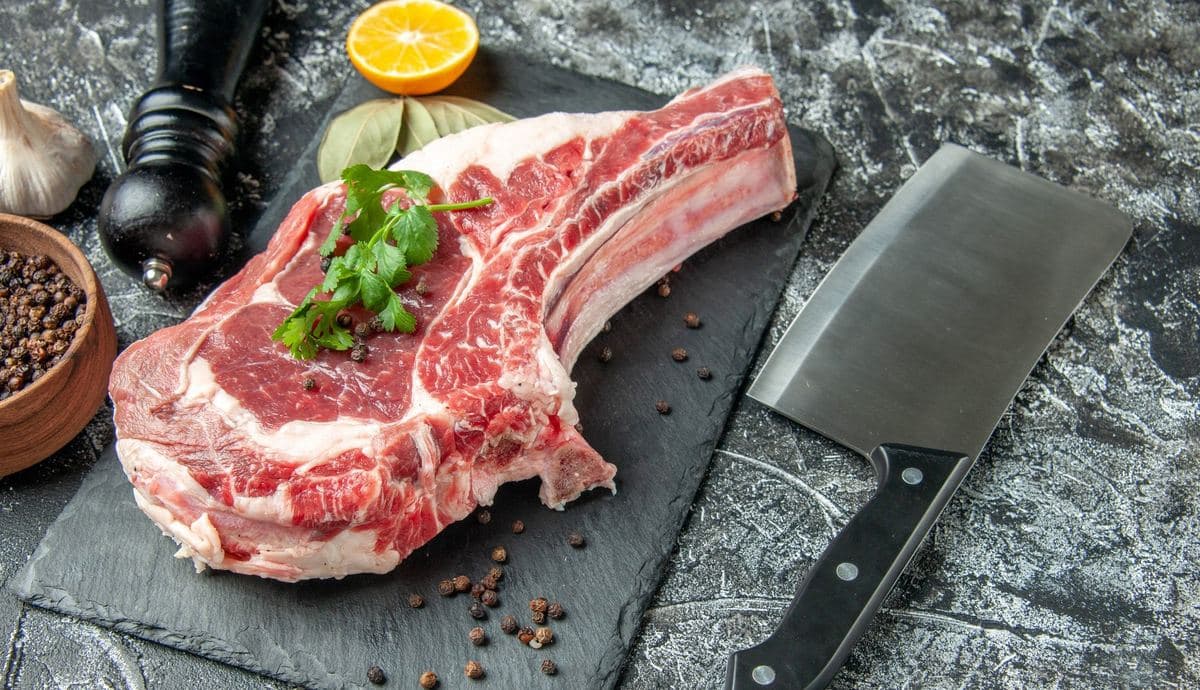 Raw rib steak with a cleaver on a slate board