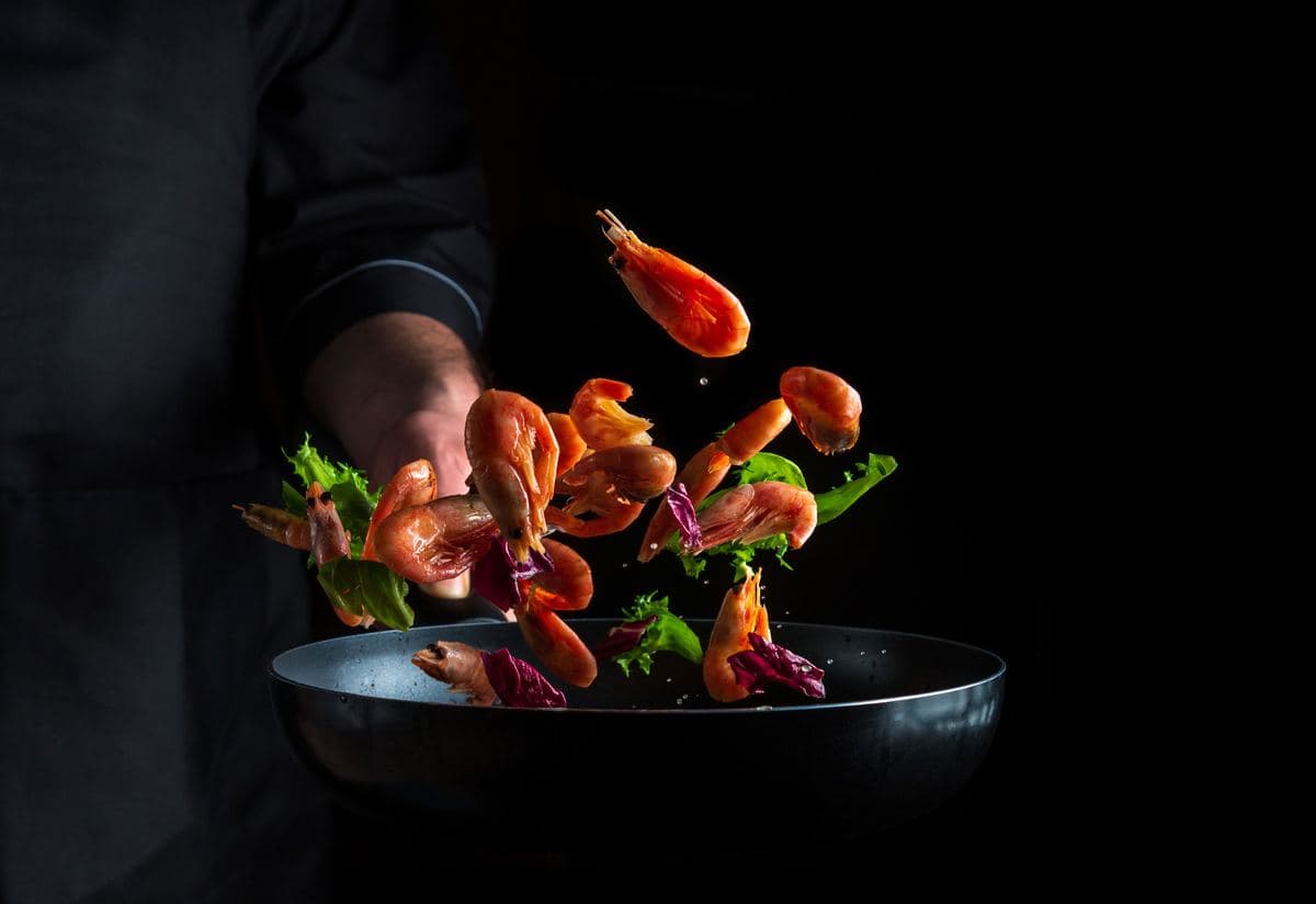Chef tossing prawns and vegetables in a pan