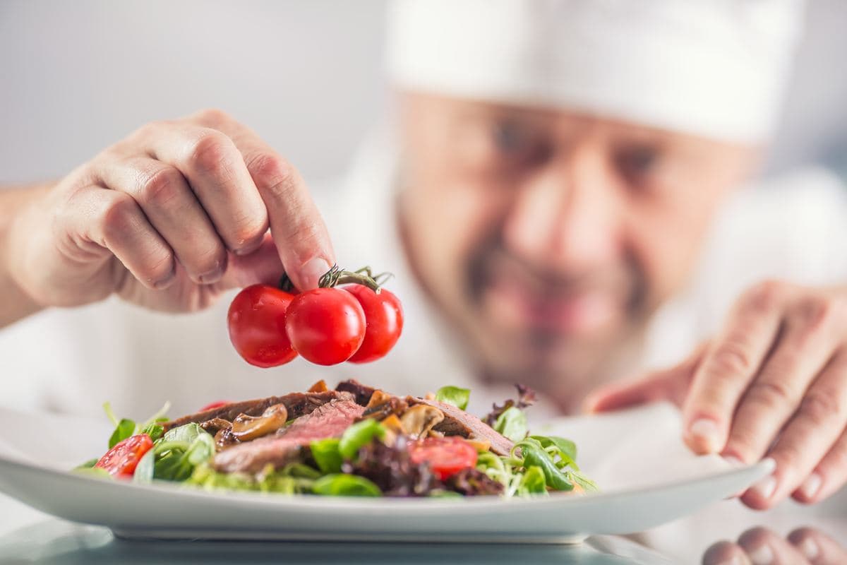 Chef in whites finishing a plated salad