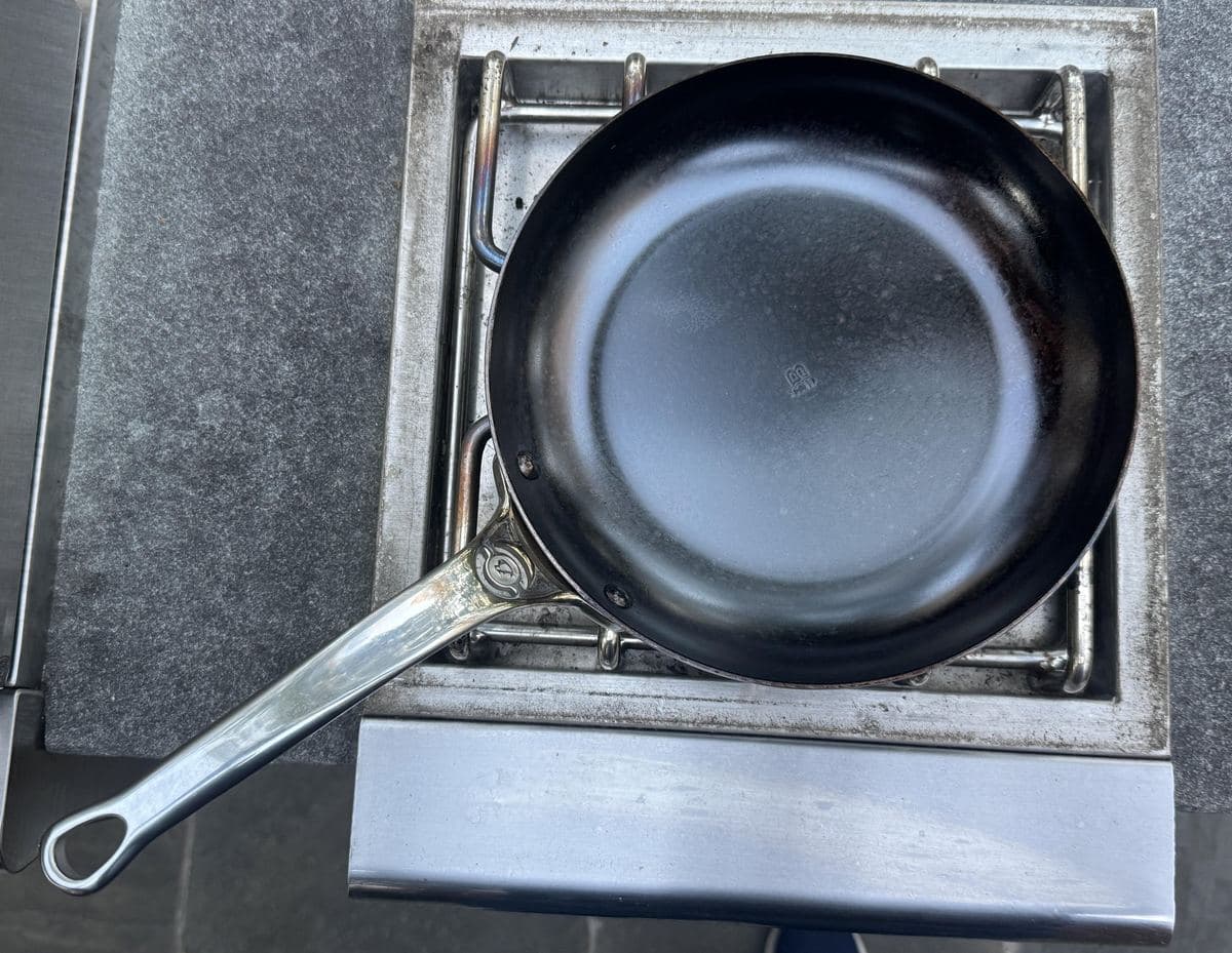 An empty carbon steel frying pan on a gas burner