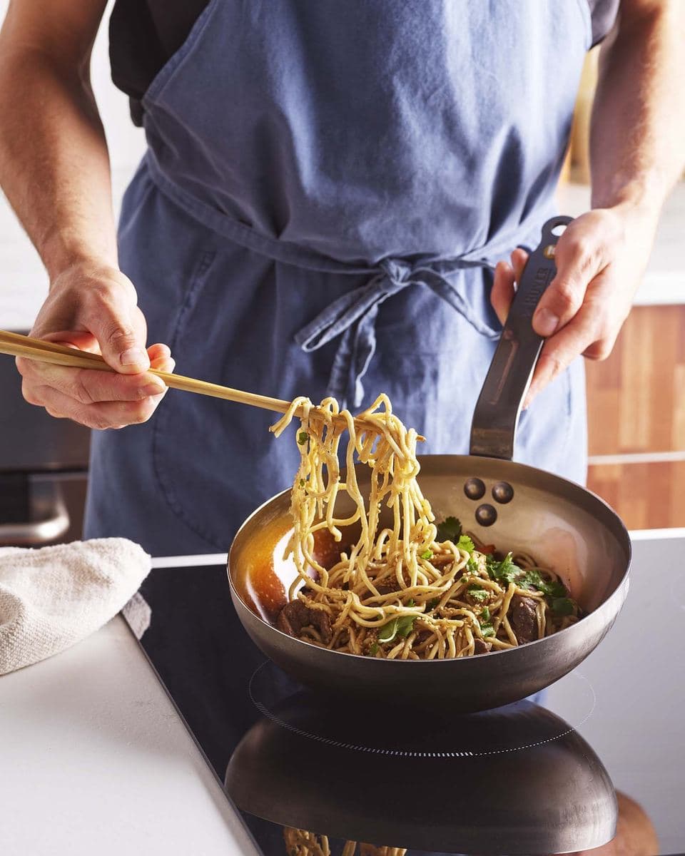 Noodles lifted with chopsticks from a carbon steel frying pan
