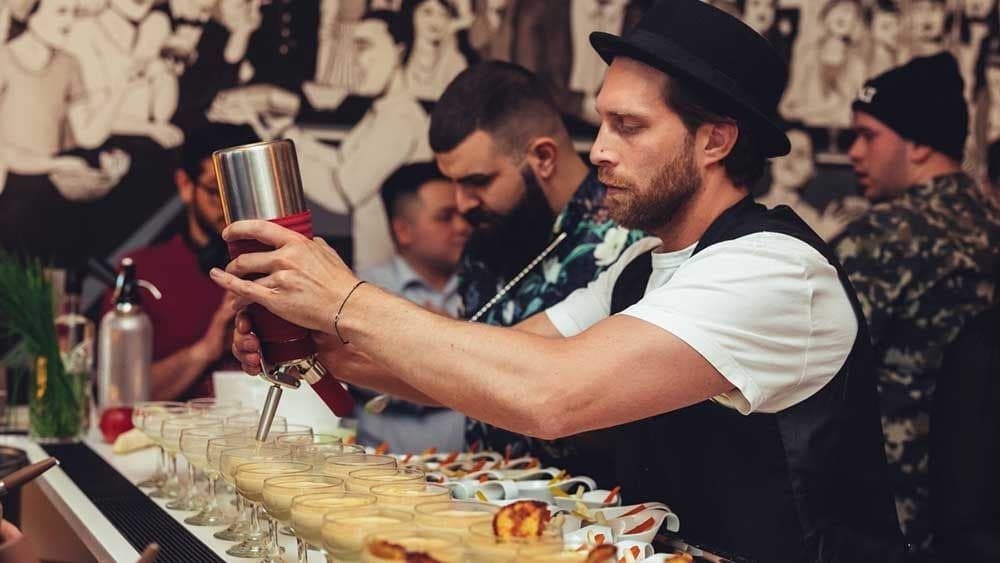 Bartender topping a row of drinks from an iSi whipper