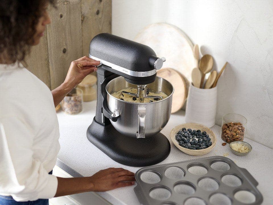 Baker using a black KitchenAid bowl-lift mixer beside a muffin tray