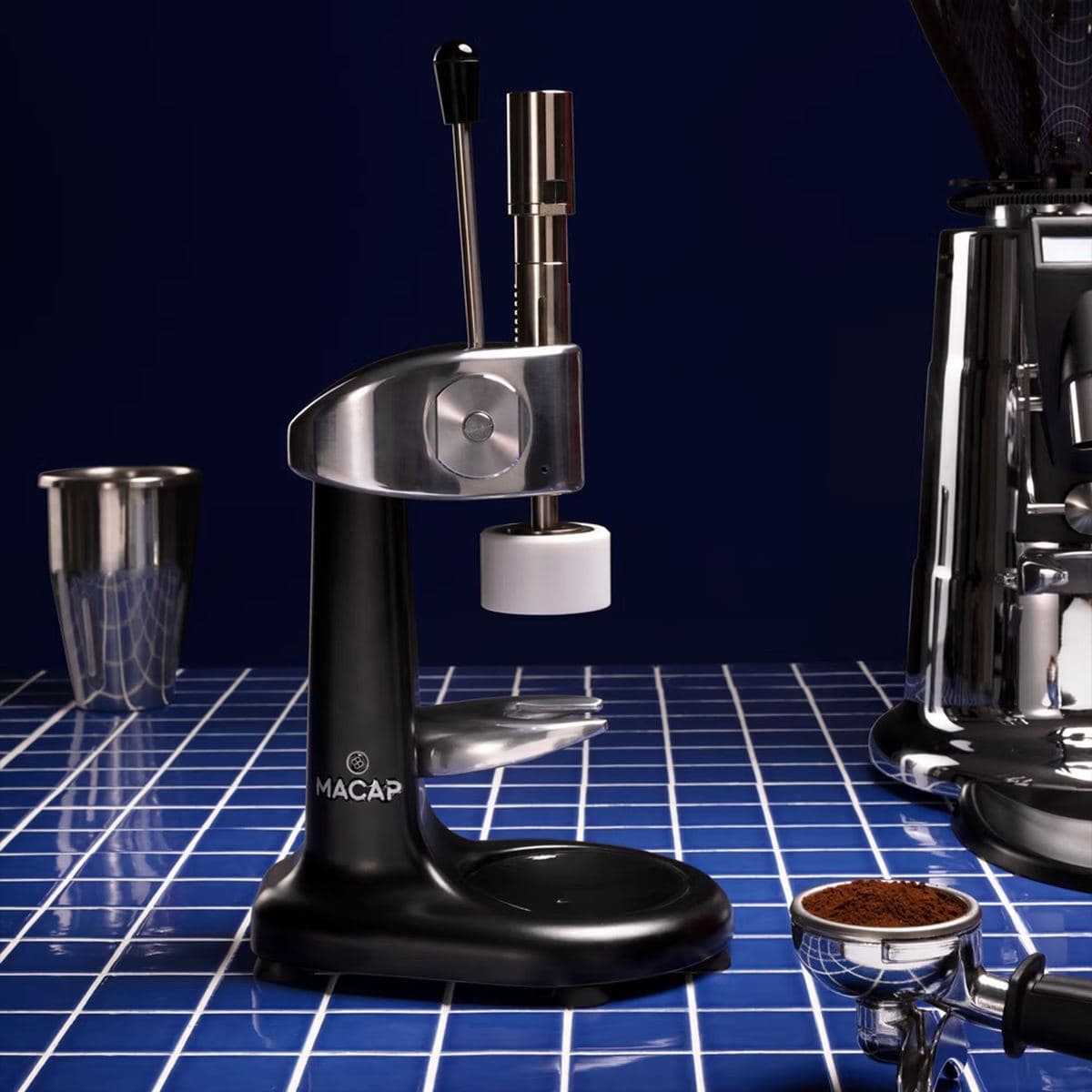 A Macap bench tamper beside a portafilter of ground coffee