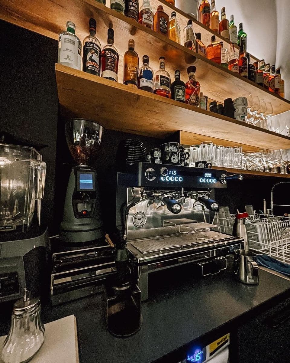A Macap grinder beside an espresso machine on a back bar