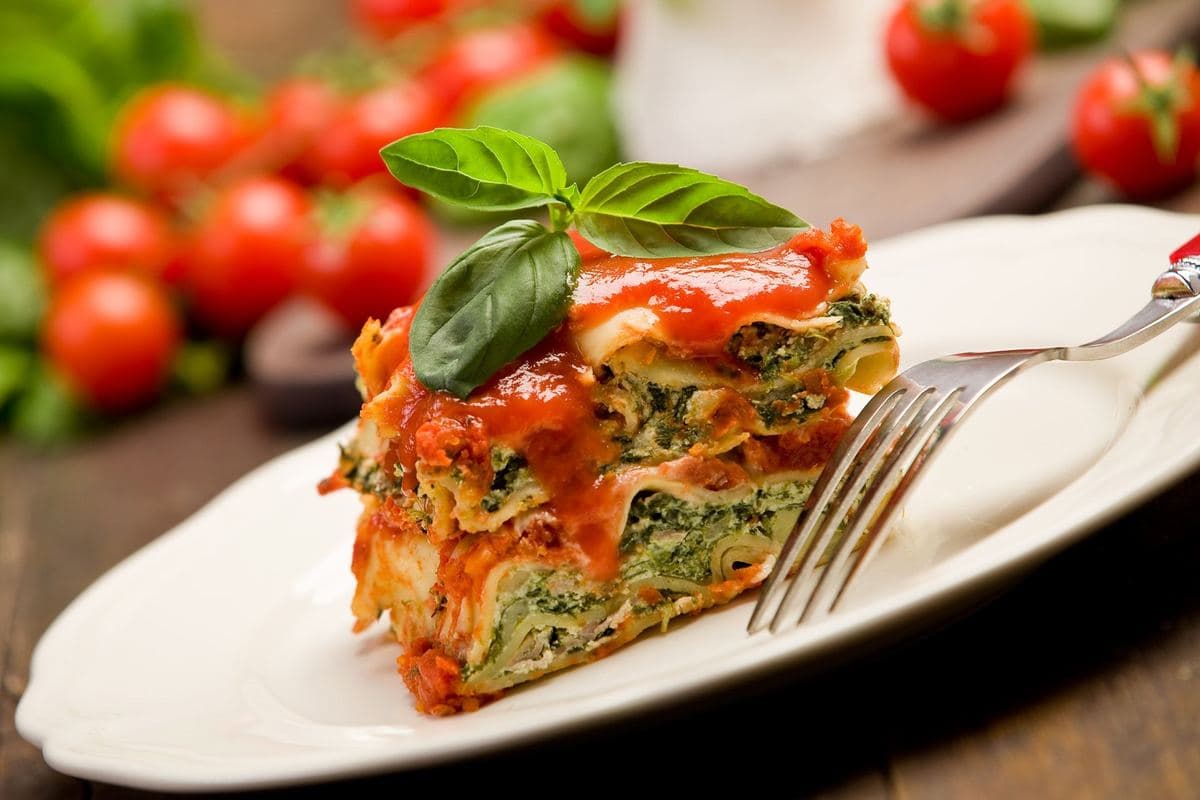 A slice of spinach lasagne with basil and cherry tomatoes
