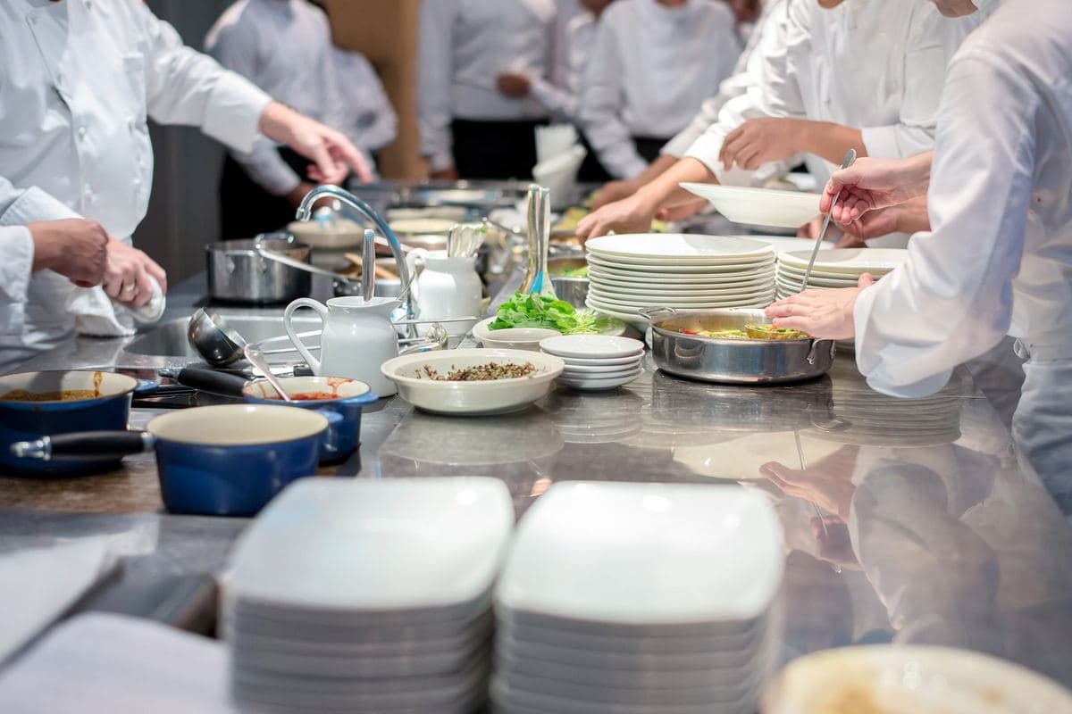 Chefs plating up along a stainless steel kitchen line