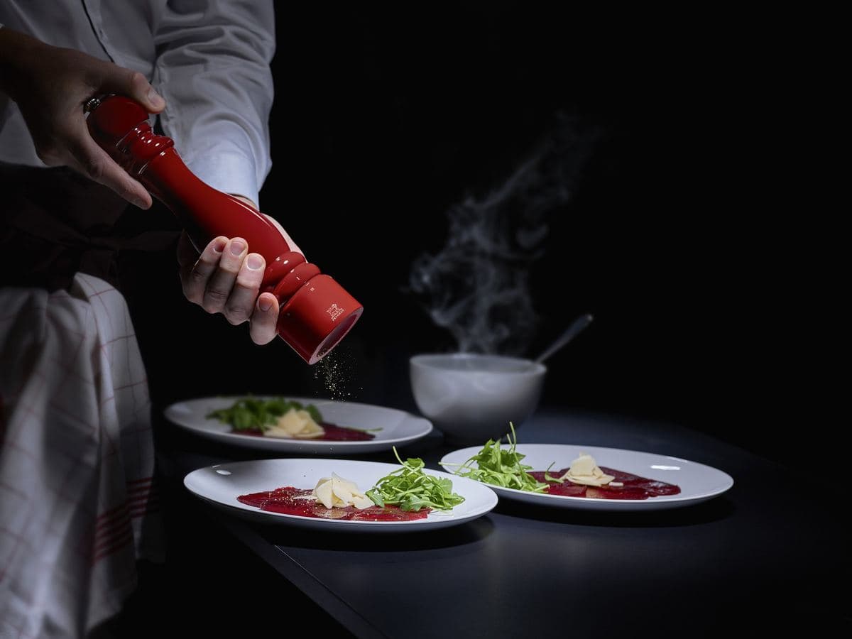 Chef seasoning plates with a red Peugeot pepper mill