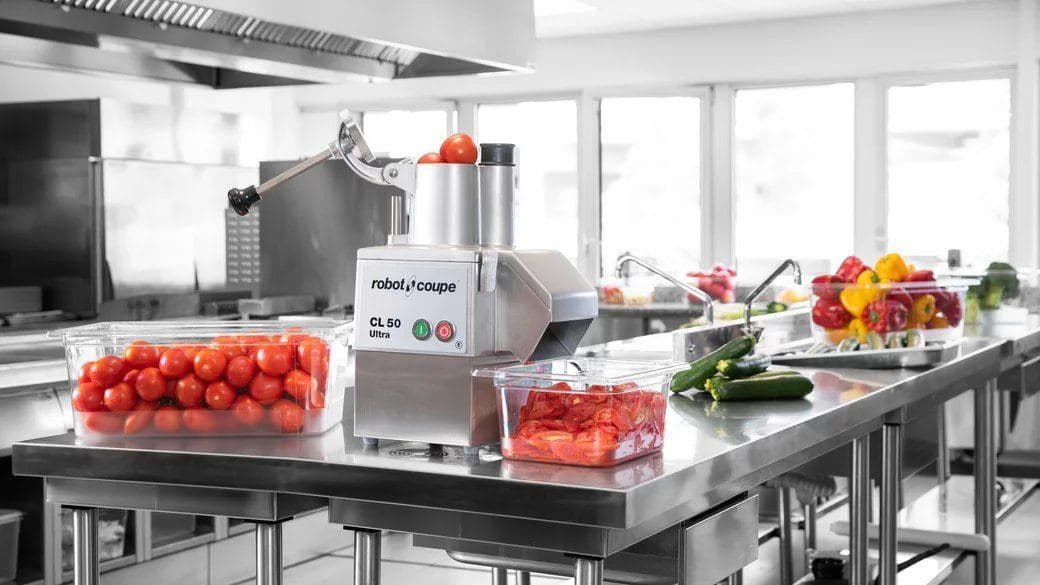 Robot-Coupe vegetable preparation machine with tomatoes and peppers on a stainless bench